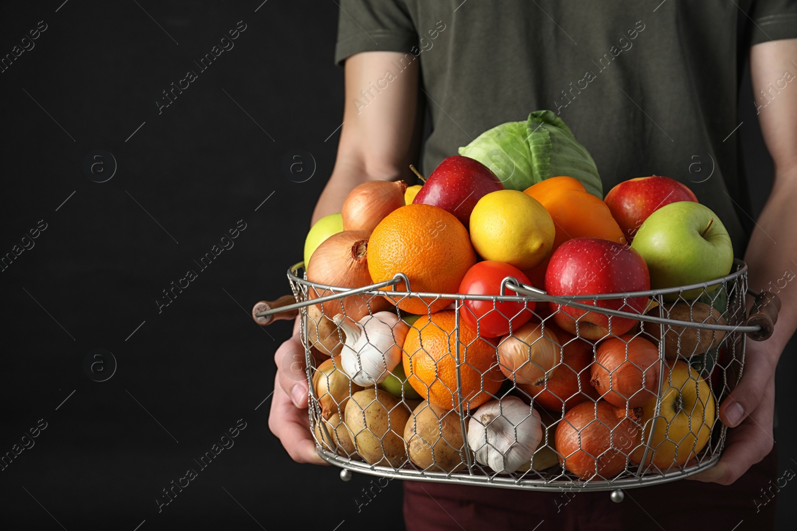 Photo of Man holding basket full of fresh  vegetables and fruits against black background, closeup. Space for text