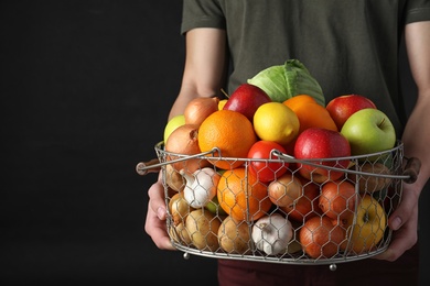 Photo of Man holding basket full of fresh  vegetables and fruits against black background, closeup. Space for text