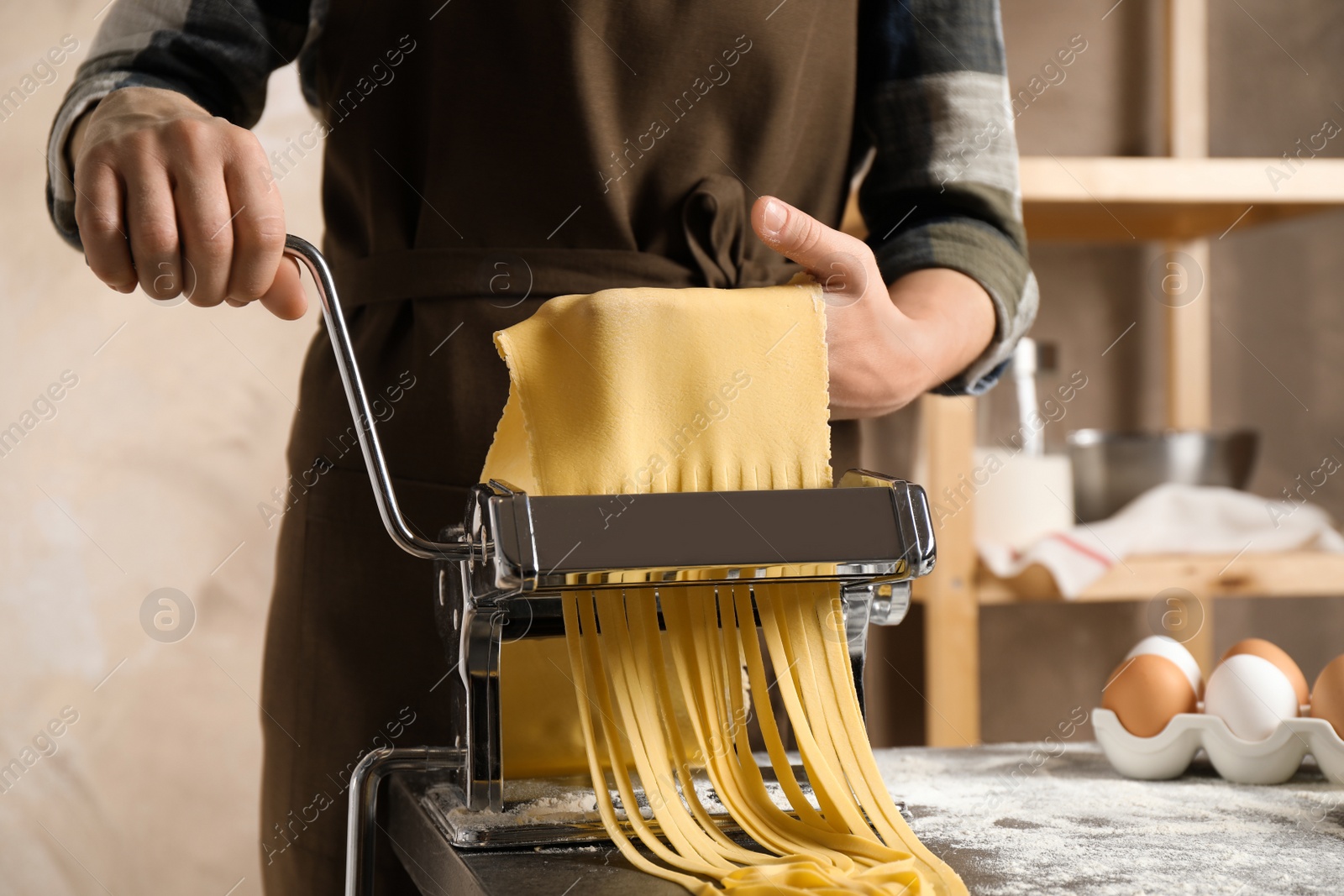 Photo of Woman preparing noodles with pasta maker machine at table indoors, closeup