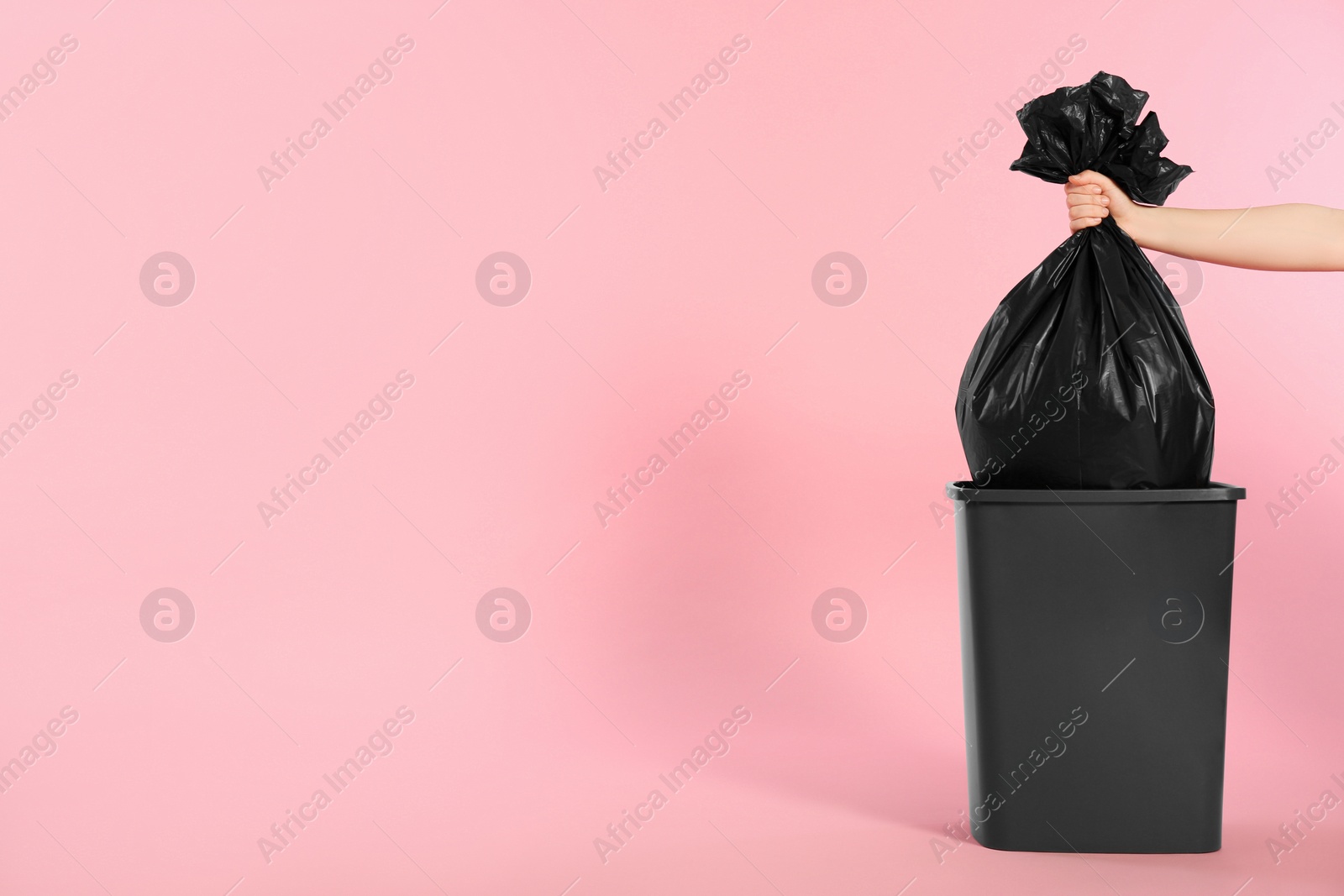 Photo of Woman holding trash bag full of garbage over bucket on pink background, closeup. Space for text