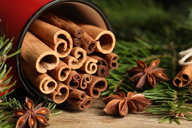 Photo of Many cinnamon sticks, anise stars and fir branches on wooden table, closeup. Aromatic spices