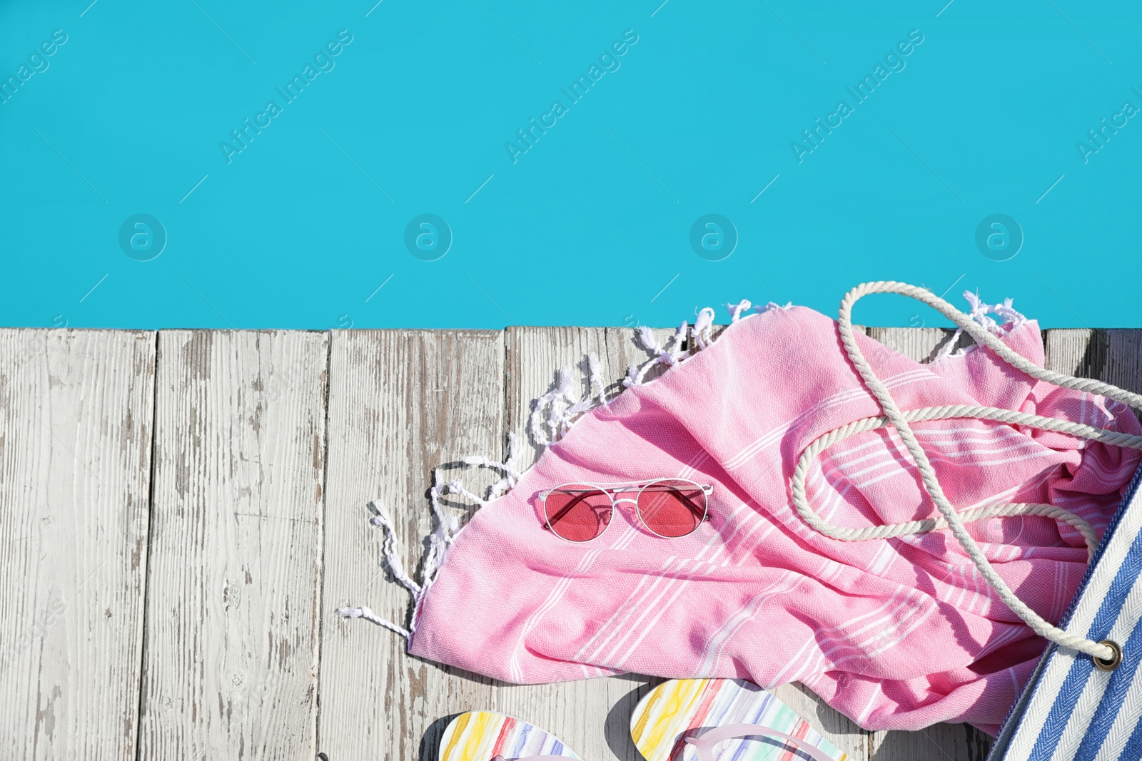 Photo of Beach accessories on wooden deck near outdoor swimming pool, flat lay. Space for text