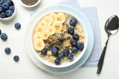 Tasty oatmeal with banana, blueberries and chia seeds served in bowl on white wooden table, flat lay