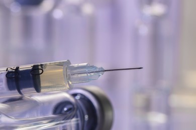 Glass vial and syringe with medication against blurred background, closeup. Space for text