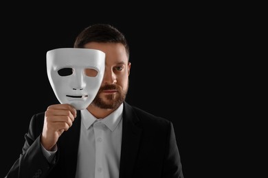 Photo of Multiple personality concept. Man covering face with mask on black background. Space for text