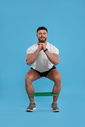 Photo of Young man exercising with elastic resistance band on light blue background