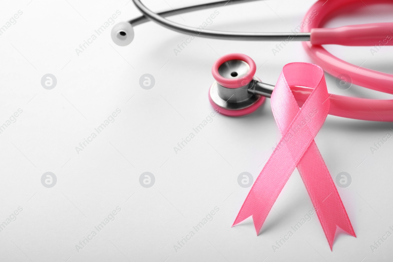 Photo of Pink ribbon and stethoscope on white background, space for text. Breast cancer concept