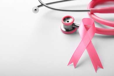 Photo of Pink ribbon and stethoscope on white background, space for text. Breast cancer concept