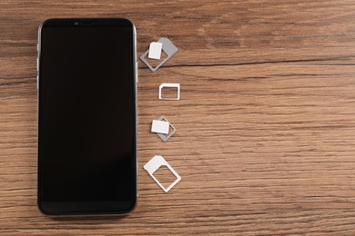 Photo of SIM cards and mobile phone on wooden table, flat lay. Space for text