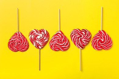 Sweet heart shaped lollipops on yellow background, flat lay. Valentine's day celebration