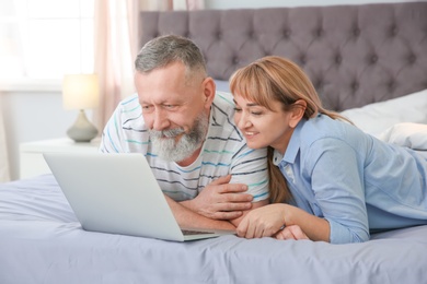 Photo of Mature couple using laptop on bed at home