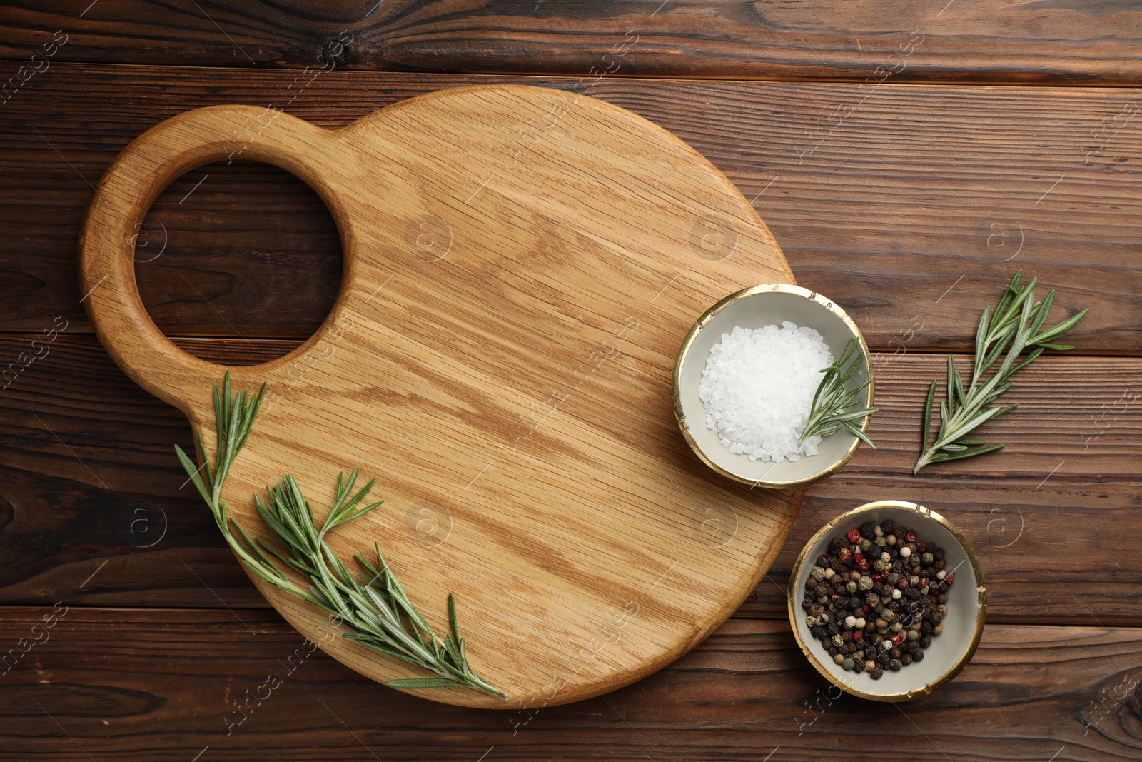 Photo of Cutting board, salt, pepper and rosemary on wooden table, flat lay. Space for text