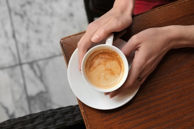 Photo of Young woman with cup of delicious coffee at table