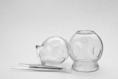 Photo of Glass cups and tweezers on light grey background. Cupping therapy