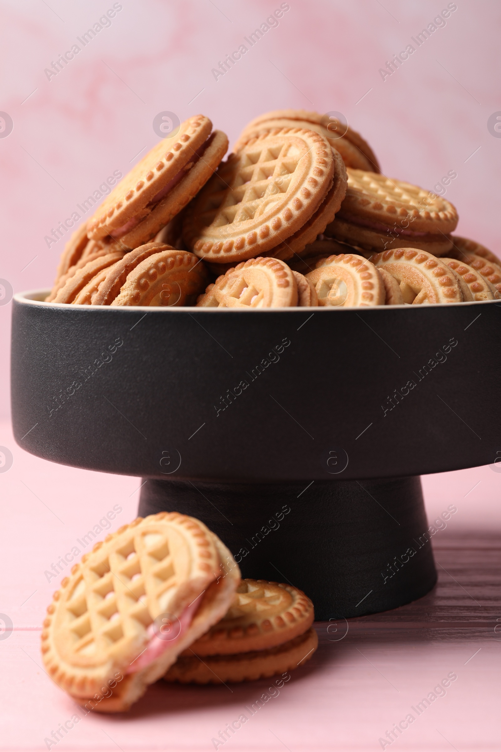 Photo of Tasty sandwich cookies with cream on pink wooden table, closeup