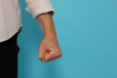 Photo of Young man showing fist on light blue background, closeup and space for text. Aggression concept