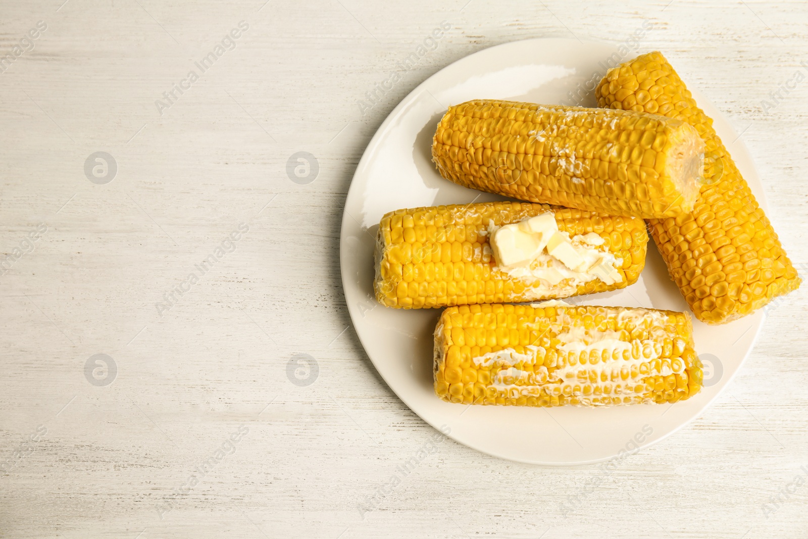 Photo of Delicious boiled corn with butter on white wooden table, top view. Space for text