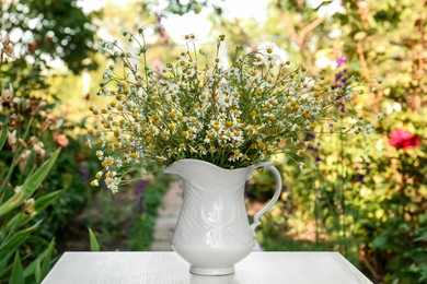 Photo of Beautiful bouquet of chamomiles in ceramic jug on white table outdoors
