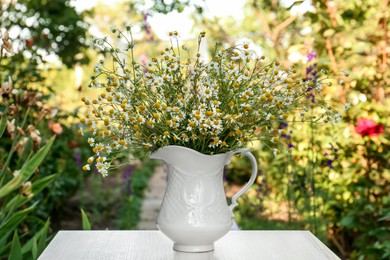 Beautiful bouquet of chamomiles in ceramic jug on white table outdoors