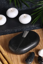Photo of Stones with acupuncture needles and burning candles on bamboo mat