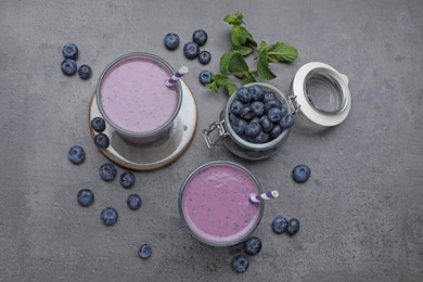 Glasses of blueberry smoothie with mint and fresh berries on grey table, flat lay