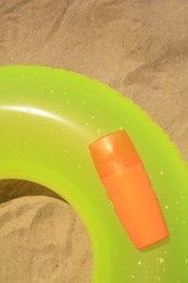 Photo of Sunscreen and inflatable ring on sand, above view. Sun protection care