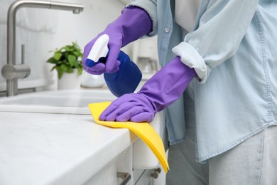 Photo of Woman cleaning white countertop with rag and detergent indoors, closeup