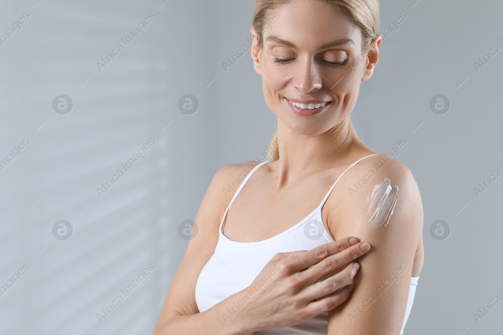 Photo of Happy woman applying body cream onto arm indoors, space for text