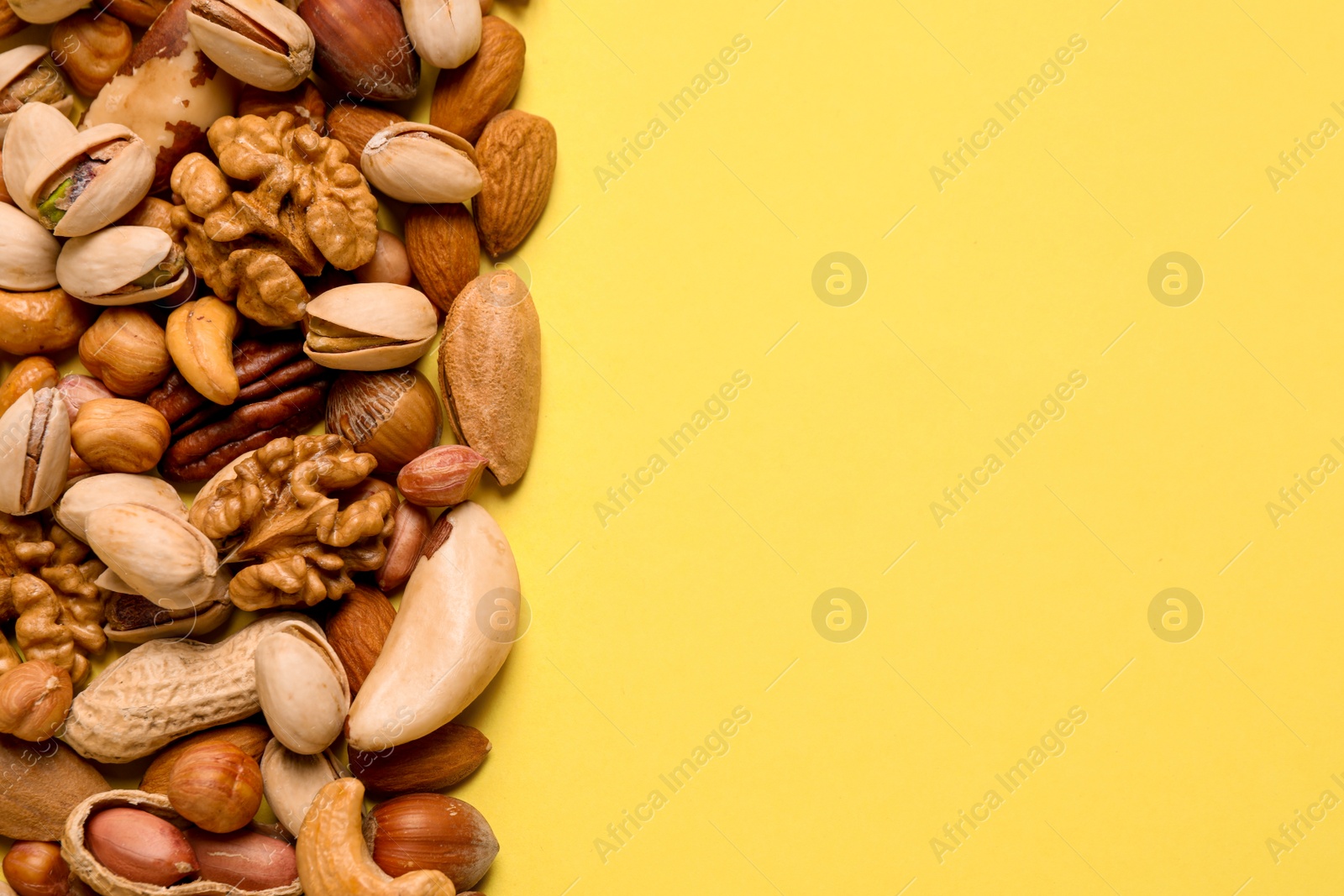 Photo of Different delicious nuts on yellow background, flat lay. Space for text