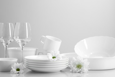 Photo of Set of many clean dishware, flowers and glasses on light table
