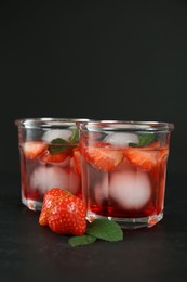 Delicious cocktails with strawberries, mint and ice balls on black table, space for text