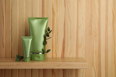 Tubes of cosmetic products and plants on shelf near wooden wall, space for text