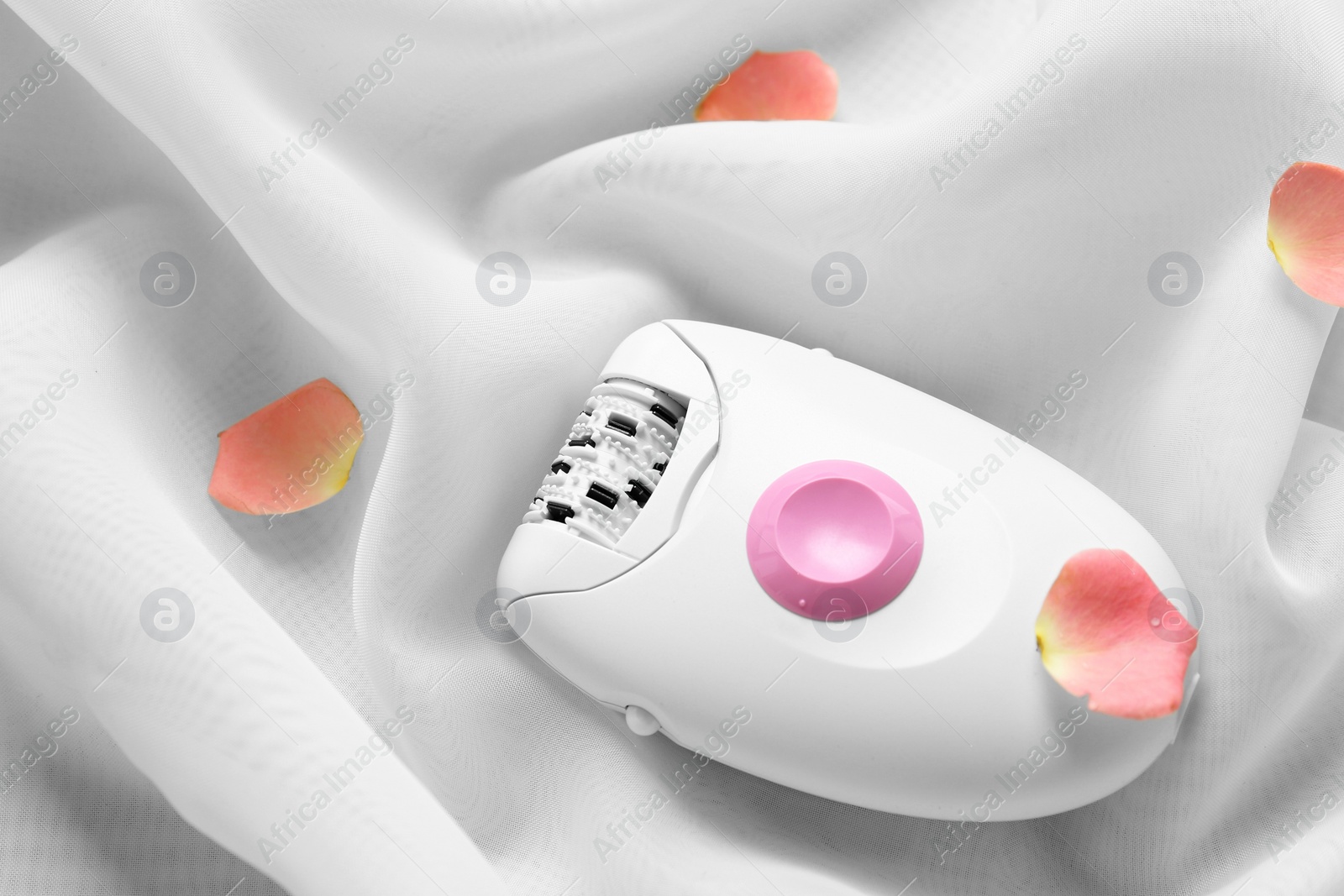 Photo of Modern epilator and flower petals on light fabric