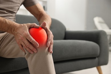 Image of Arthritis symptoms. Man suffering from pain in his knee on sofa indoors, closeup. Space for text