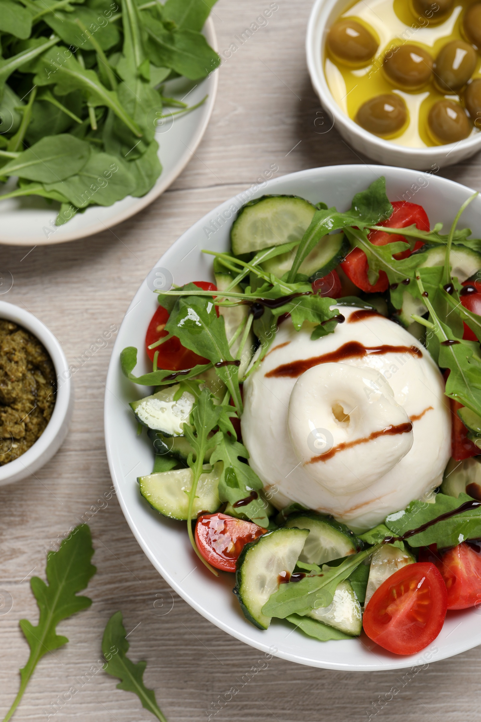 Photo of Delicious burrata salad served on wooden table, flat lay