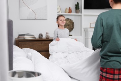 Brother and sister changing bed linens together in bedroom