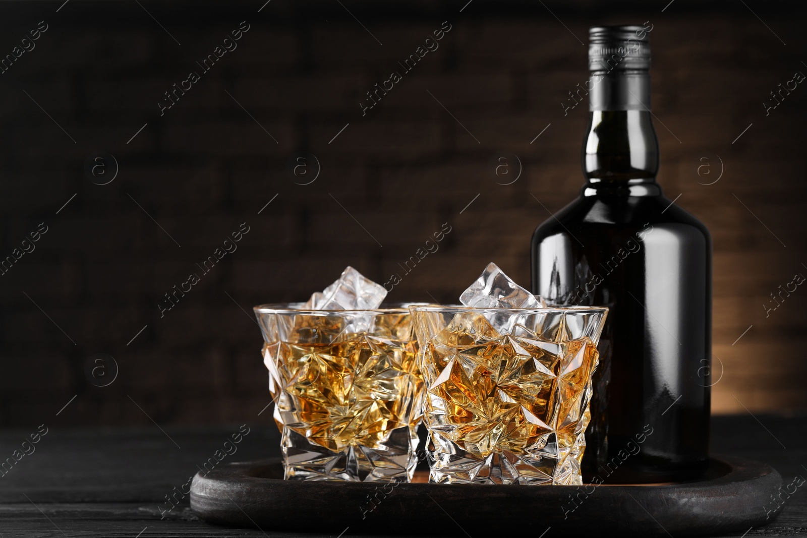 Photo of Whiskey with ice cubes in glasses and bottle on black wooden table