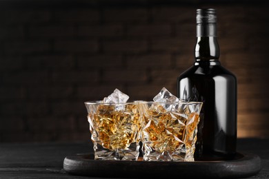 Whiskey with ice cubes in glasses and bottle on black wooden table