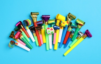 Colorful party blowers on light blue background, flat lay