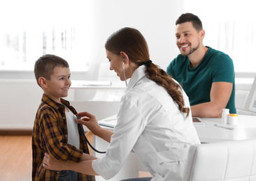 Photo of Father and son visiting pediatrician. Doctor examining little patient with stethoscope in hospital
