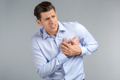 Young man suffering from chest pain on grey background