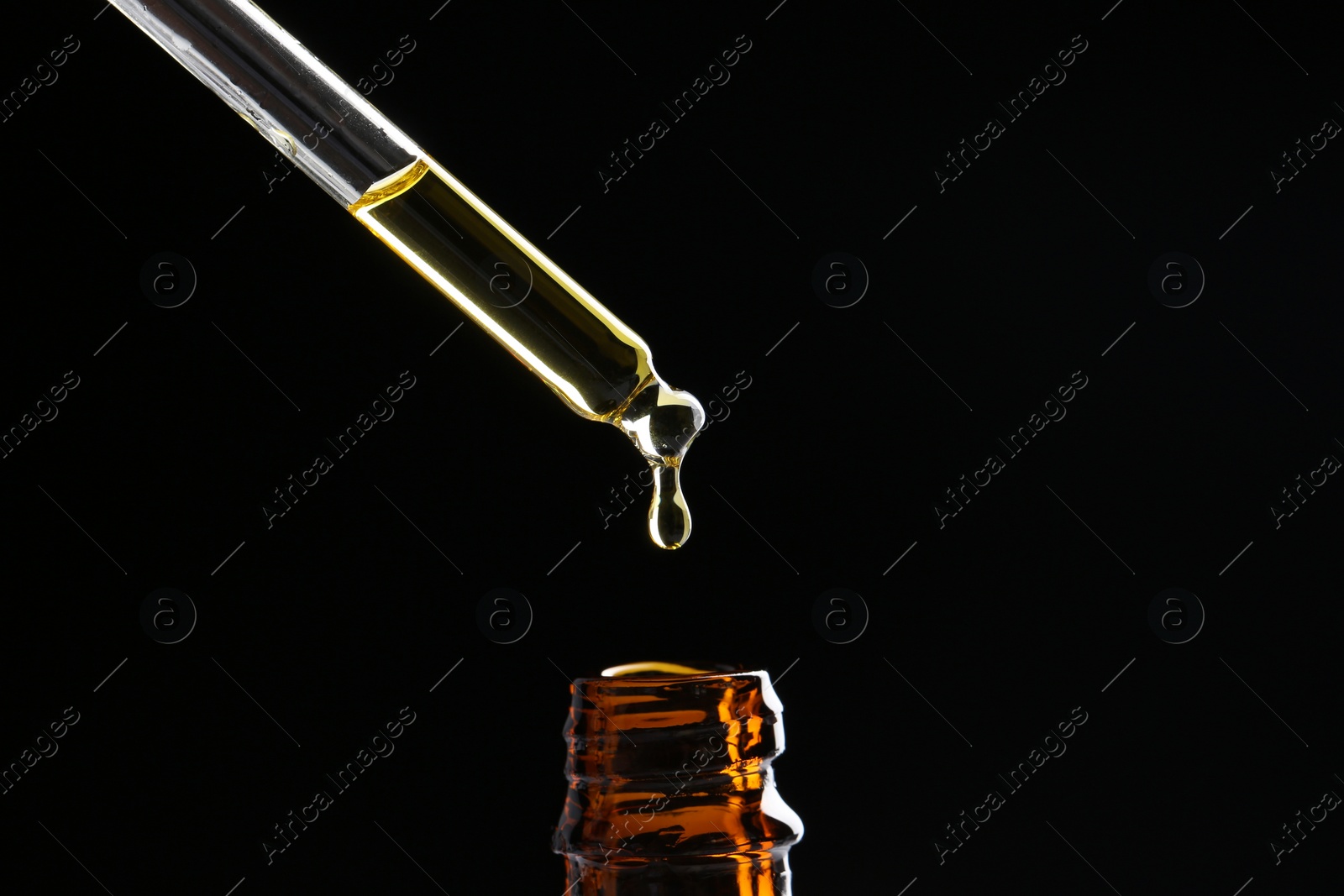 Photo of Dripping tincture from pipette into bottle on black background, closeup