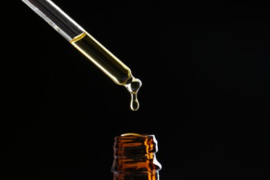 Photo of Dripping tincture from pipette into bottle on black background, closeup