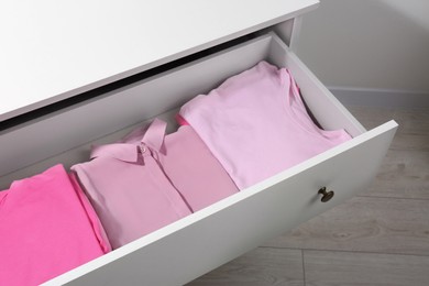Many folded pink clothes in white chest of drawers indoors