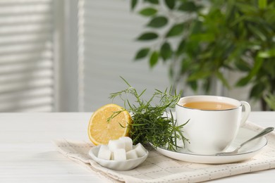 Photo of Aromatic herbal tea, fresh tarragon sprigs, sugar cubes and lemon on white wooden table, space for text