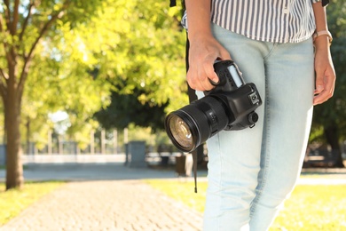 Young female photographer with professional camera in park. Space for text