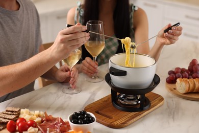 Photo of Couple enjoying cheese fondue during romantic date indoors, closeup