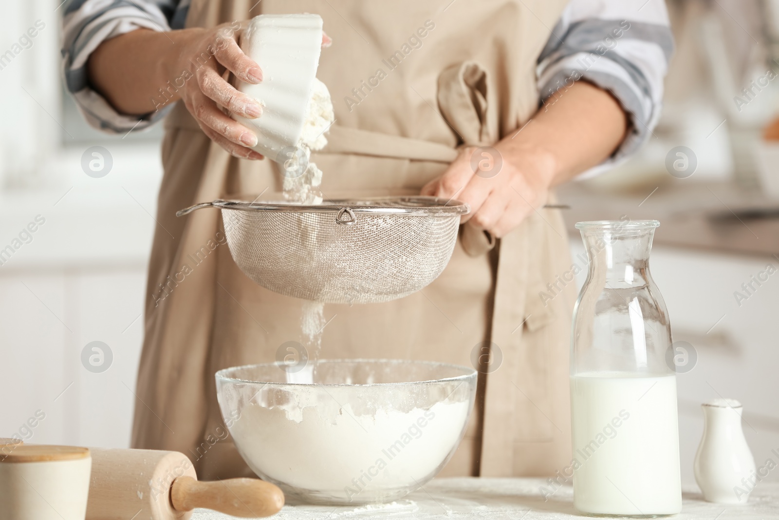 Photo of Woman sifting flour into bowl on table in kitchen