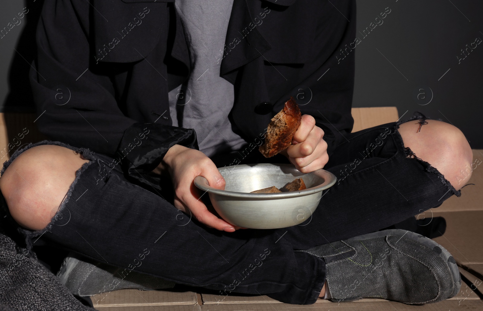 Photo of Poor woman with bread sitting on floor near dark wall, closeup