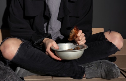 Poor woman with bread sitting on floor near dark wall, closeup